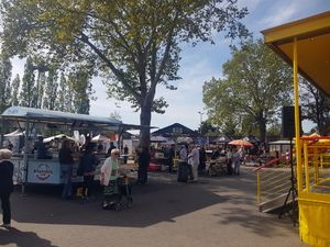 Stände und Besucher unter Bäumen auf dem Gelände