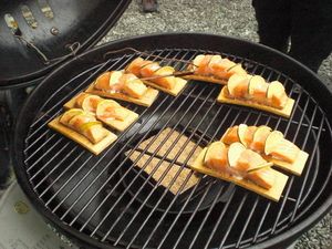 Lachsstücke auf Holzbrettchen auf dem Rost eines Kugelgrills