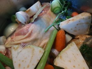 Suppenhuhn mit Gemüse und Kräutern im Topf