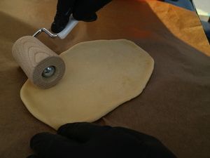 Flammkuchenteig wird mit dem Nudelholz ausgerollt
