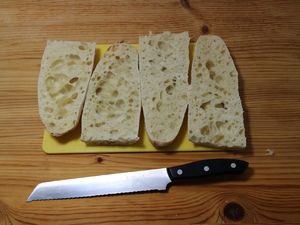Längs halbierte Baguettestücke auf einem Brett mit Brotmesser