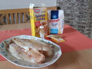 Fischfilets auf einem Teller, dahinter Mehl und Speisestärke