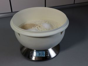 Plastikschüssel mit Mehl, Hefe, Salz und Zucker auf einer Küchenwaage