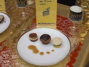 Dessertteller mit drei Törtchen vor einem Schild mit Tortenstück