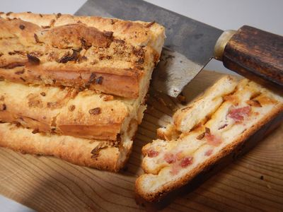 Aufgeschnittenes Zwiebelbrot mit Speck auf einem Brett