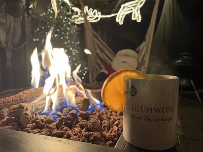 Becher Glühwein mit Orangenscheibe neben einer Feuerstelle