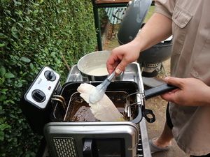 Backfisch wird mit der Zange in die Fritteuse gelegt